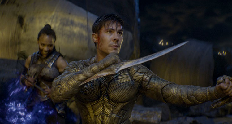 Mortal Kombat 2021 Movie Lewis Tan as Cole Young in his suit holding blades as Sisi Stringer as Mileena teleports behind him