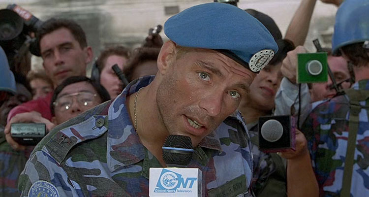Street Fighter 1994 Movie Scene Jean-Claude Van Damme as Colonel Guile holding a mic and talking to the screen while wearing camo and a blue beret