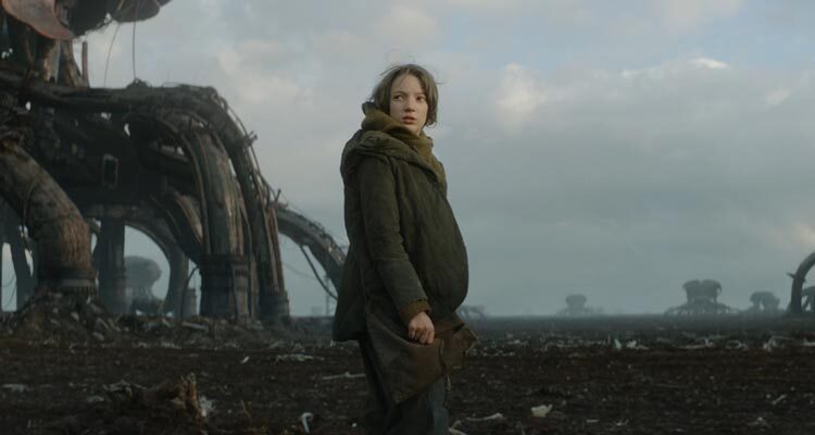 Vesper 2022 Movie Scene Raffiella Chapman as Vesper roaming the wasteland with giant structure behind her