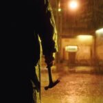 Open 24 Hours 2018 Movie Scene A killer in a raincoat holding a hammer in the rain in front of a remote gas station